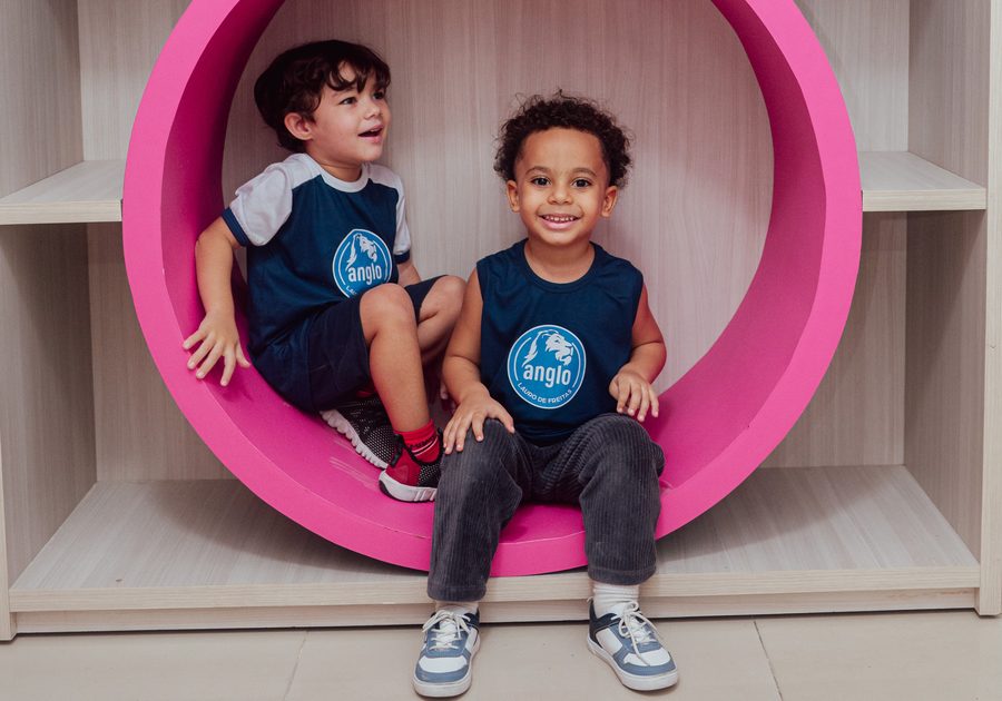 Duas crianças da Educação Infantil sentadas no nicho redondo cor-de-rosa da brinquedoteca
