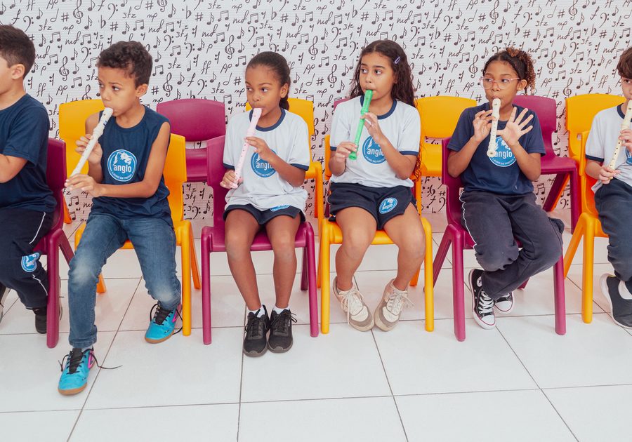Alunos tocando flauta doce sentados em cadeiras coloridas na sala de música