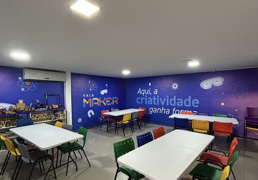 Sala maker com mesas de trabalho, cadeiras coloridas e painel escrito Aqui, a criatividade ganha forma